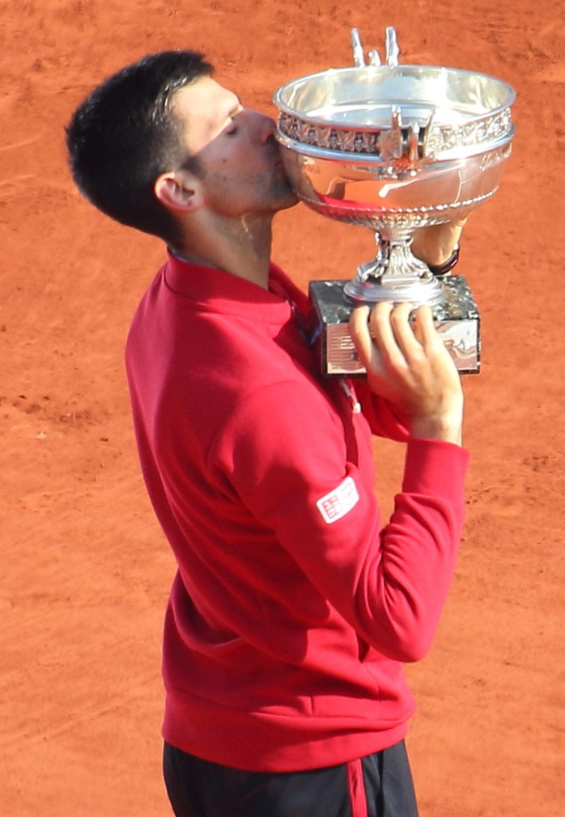 Novak Djokovic feiert mit dem French-Open-Pokal nach Sieg gegen Rafael Nadal im Finale der Herren-Einzel, hält und küsst den Pokal mit einem triumphierenden Gesichtsausdruck.