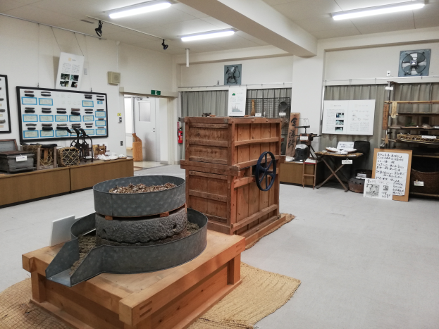 Eine Werkstatt im Nationalen Naturhistorischen Museum voller verschiedener Maschinen, ein hölzerner Kasten mit Rädern, ein hölzerner Tisch mit Gegenständen, ein Teppich, Tafeln mit Text, Gestelle mit Gegenständen, ein Feuerlöscher, eine Tür, Vorhänge, eine Wand und eine Decke mit Lampen.