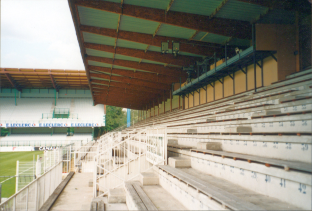 Altes Foto eines Stadions mit Sitzreihen, Geländern, Treppen, einem Schuppen, Informationsschildern, Gras, Bäumen und Himmel.
