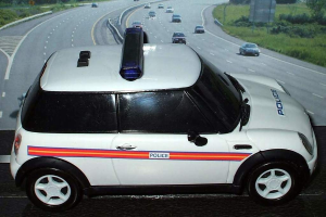 Weißes Polizeiauto vor dem fließenden Verkehr auf einer grünen Straße mit Bäumen außerhalb der Stadt.