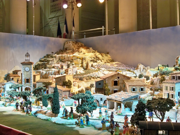 Ein detailliertes Krippenmodell im Museum ausgestellt, mit Figuren, Gebäuden, Naturlementen und dekorativen Lichtern.