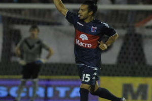 Ein Fussballspieler feiert auf dem Boden nach einem Tor, mit jubelnden Zuschauern und einer Person im Hintergrund, alles vor einem unscharfen, dynamischen Hintergrund.