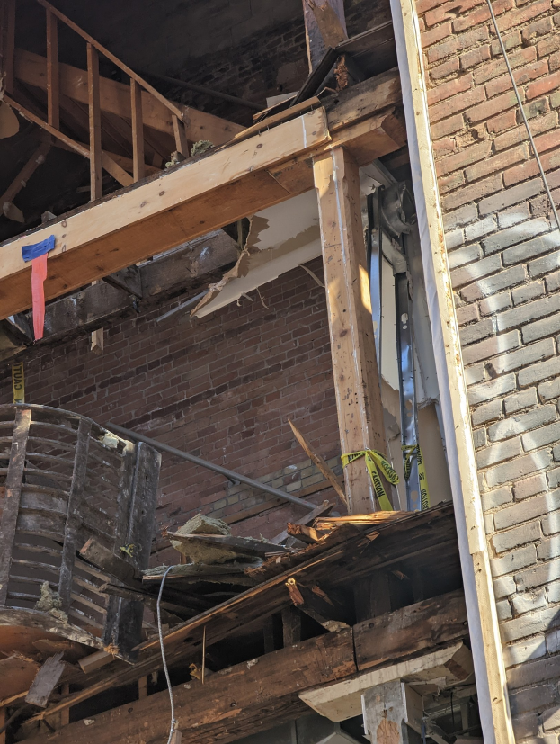 Teilweise abgerissenes Gebäude mit verstreuten Holzplanken, Schutt, zerbrochenen Fenstern und Türen.