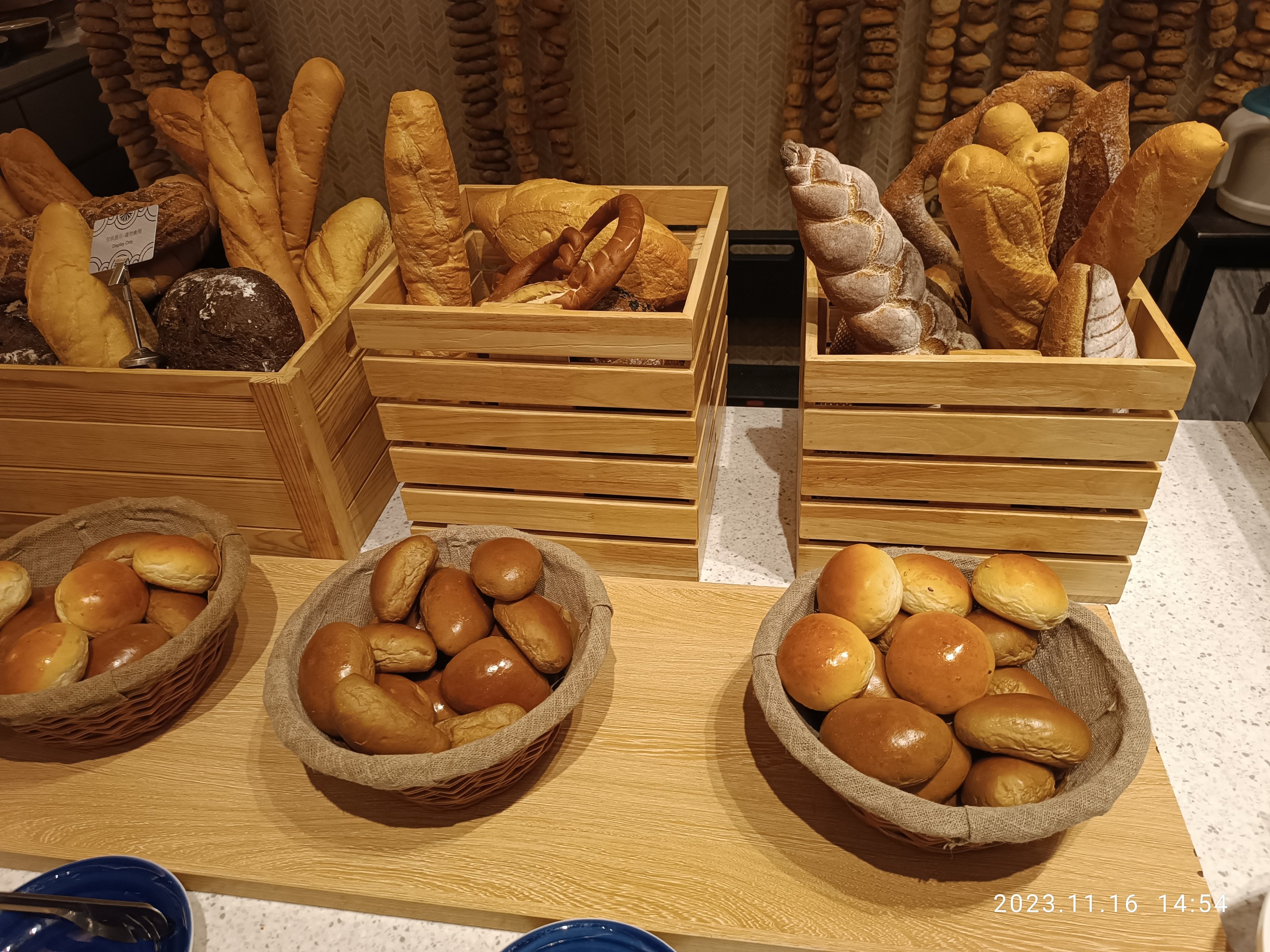 Holztisch mit Körben voller Brot, Tellern und Löffeln in einer Pariser Bäckerei mit einer wasserzeichenverzierten Wand.
