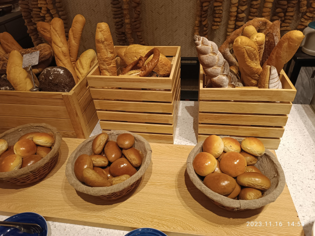 Holztisch mit Körben voller Brot, Tellern und Löffeln in einer Pariser Bäckerei mit einer wasserzeichenverzierten Wand.