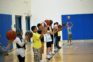 Gruppe junger Menschen auf einem Basketballfeld mit Basketballs, mit Türen und einer Wand im Hintergrund.