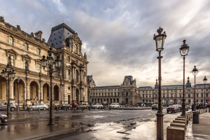 Das ikonische Louvre-Museum in Paris, Frankreich, mit seinen historischen Gebäuden, der Straßeninfrastruktur, fahrenden Fahrzeugen, Passanten und bewölktem Himmel.