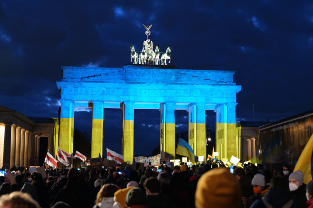 Menge mit Fahnen und Schildern vor dem Brandenburger Tor in Berlin, mit einer Fahne auf der rechten Seite.