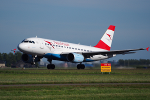 Ein Airbus A320-200 der Austrian Airlines startet vom Frankfurter Flughafen, mit einer Texttafel, Gras, Bäumen, Gebäuden und einem klaren blauen Himmel im Hintergrund.