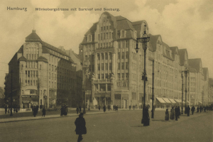 Schwarz-weiß-Foto von Menschen, die eine Straße in Hamburg, Deutschland, entlanggehen, gesäumt von Gebäuden, Straßenlaternen, Lampen und Kraftfahrzeugen unter einem bewölkten Himmel.