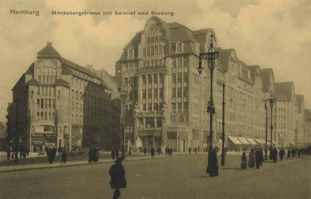 Schwarz-weiß-Foto von Menschen, die eine Straße in Hamburg, Deutschland, entlanggehen, gesäumt von Gebäuden, Straßenlaternen, Lampen und Kraftfahrzeugen unter einem bewölkten Himmel.