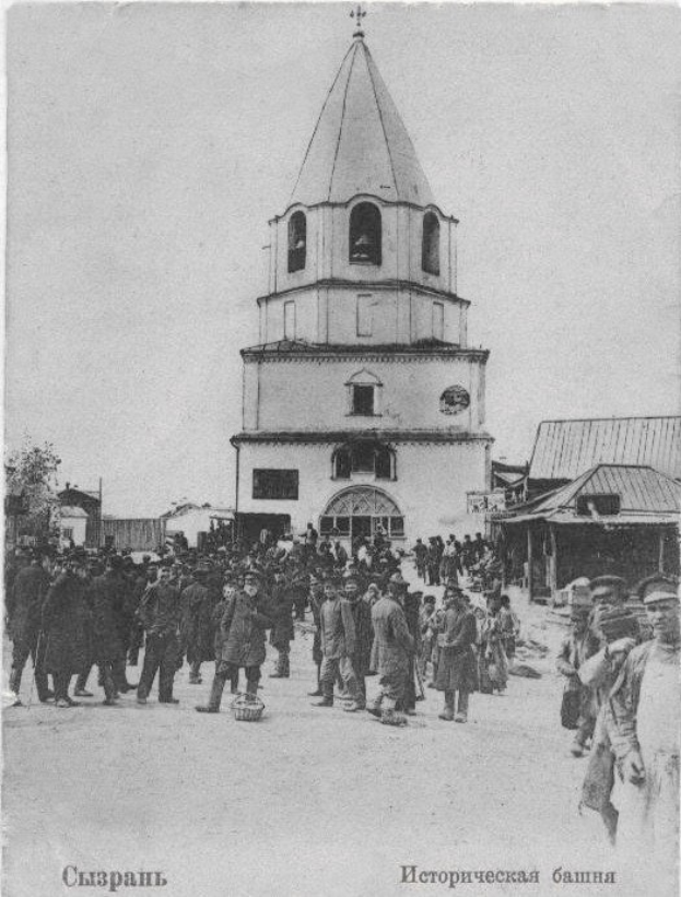 Schwarzes und weißes Foto einer Gruppe von Menschen, die vor der Intercessionskirche auf der Nerl stehen, mit Häusern und Bäumen im Hintergrund.