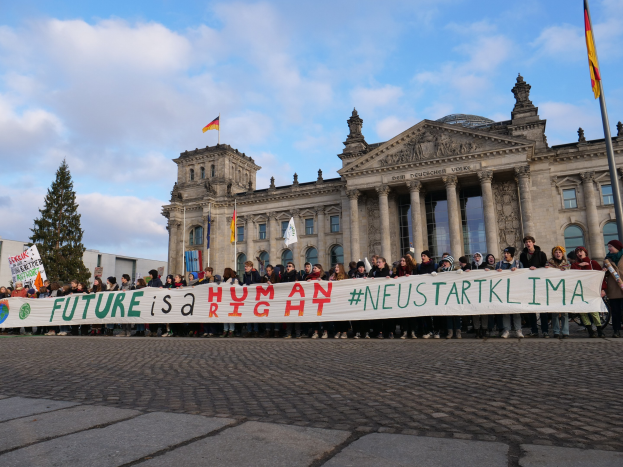 Gruppe von Menschen vor dem Reichstagsgebäude in Berlin mit einem Banner, auf dem 'Zukunft ist ein Menschenrecht' steht