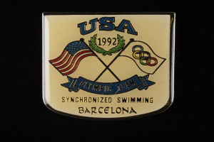 Abzeichen mit dem Text "USA Olympische Mannschaft Synchronschwimmen Barcelona" und zwei Flaggen (rot und blau) auf schwarzem Hintergrund.