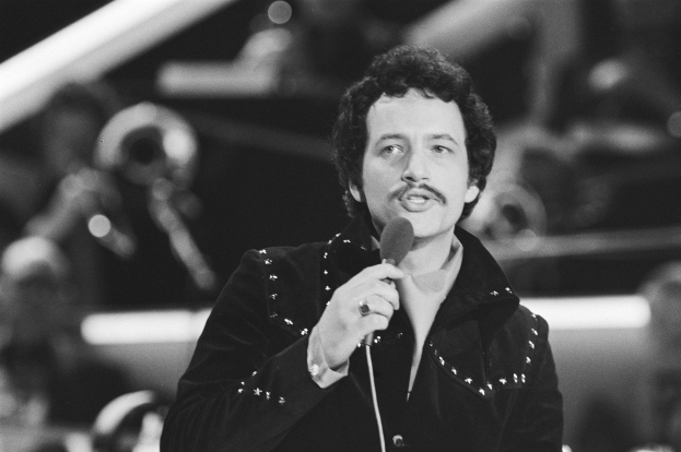 Schwarzes und weißes Foto von Elvis Presley, der ein Mikrofon während eines Live-Auftritts hält, mit einem unscharfen Hintergrund.