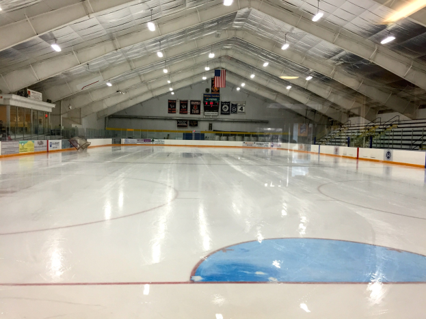 Große Indoor-Eisfläche mit Deckenbeleuchtung, Werbetafeln, Treppen mit Geländern und wenigen Menschen, wahrscheinlich eine Hockey-Anlage.