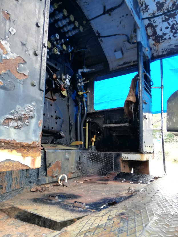 Das Innere eines verrosteten, baufälligen Lkw mit sichtbaren Gebrauchsspuren, vor dem Hintergrund von Bäumen und einem klaren blauen Himmel.
