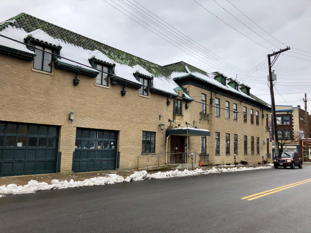 Ein großes Backsteingebäude mit einem grünen Dach an einer Straßenecke, identifiziert als die ehemalige Feuerwache St. Louis, umgeben von Fahrzeugen, Schnee, Strommasten, Bäumen und einem bewölkten Himmel.