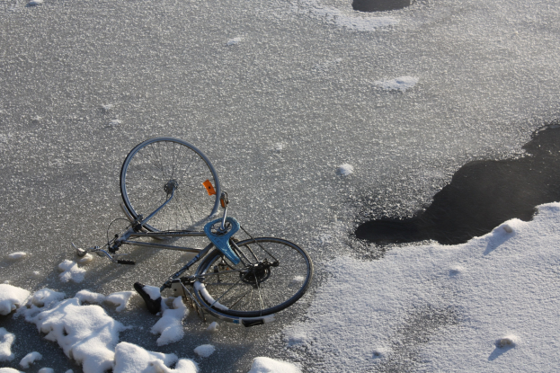 Ein Fahrrad liegt im Schnee neben einer Pfütze Wasser, umgeben von einer Schneedecke.