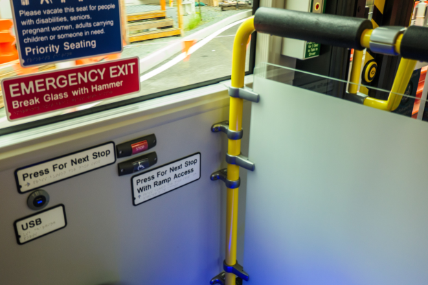 Notausgangsschild an einer Zugseite mit einer TГјr, Griff und Glasfenster, das AuГџenelemente wie eine StraГџe und Masten zeigt.