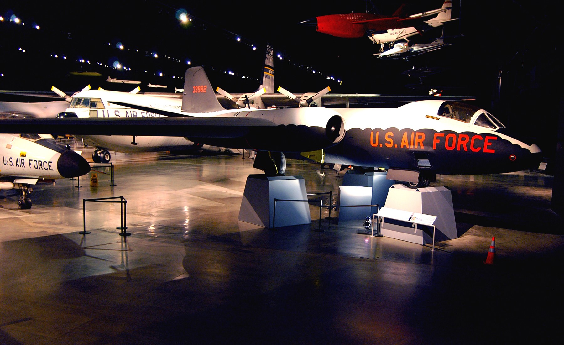 Eine Gruppe von Kampfflugzeugen in einem düster beleuchteten Museum mit St├Ąnden, Verkehrskegeln und anderen Bodenobjekten im Hintergrund.