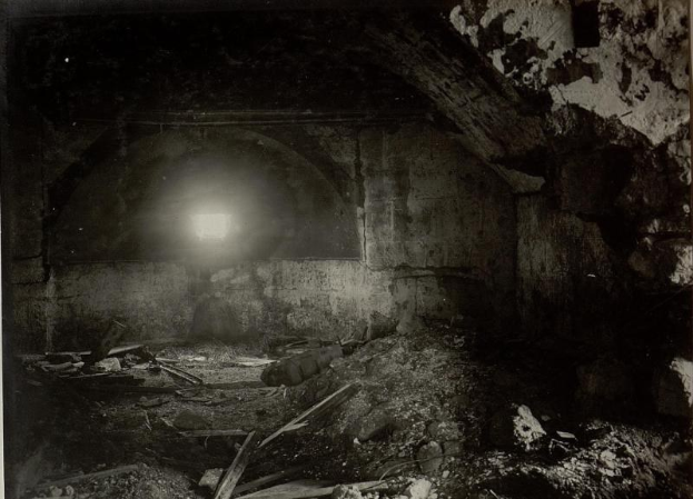 Ein Schwarz-Weiß-Foto eines zerfallenden Tunnels in den Berliner Mauertrümmern mit Schutt auf dem Boden und einem Licht am Ende.