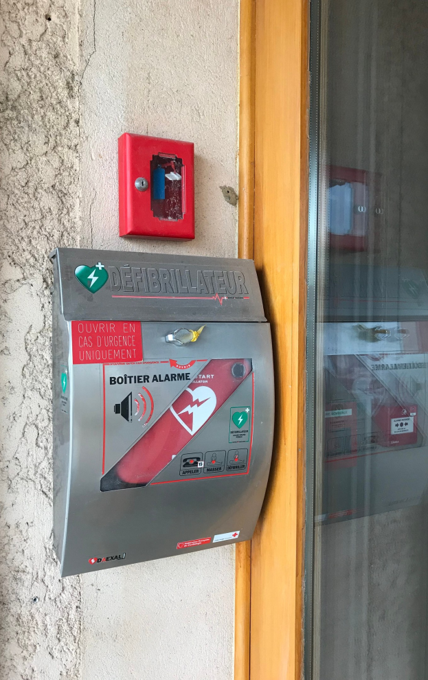 Eine rote Feueralarmanlage mit einer Glastür auf der rechten Seite, die an der Seite eines Gebäudes montiert ist und auch ein Defibrillatorgerät ist.