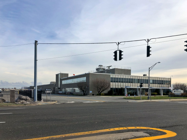 Großes Gebäude mit mehreren Ampeln, Straßenlaternen und elektrischer Infrastruktur, umgeben von Kraftfahrzeugen und Bäumen, mit einem bewölkten Himmel im Hintergrund; das Gebäude ist die neue Zentrale der Nationalen Sicherheitsbehörde.