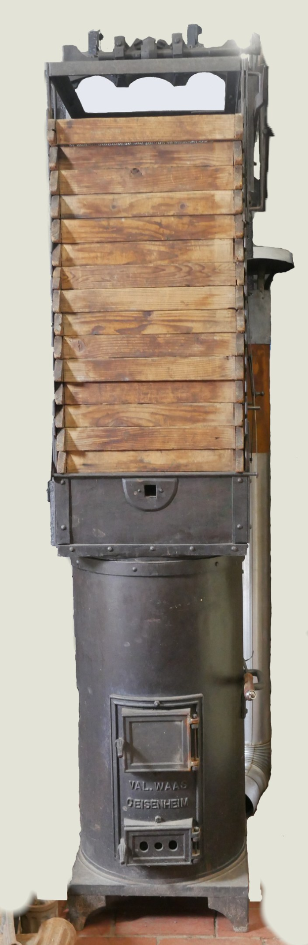 Alte Holzofen mit Metall- und Holzkonstruktion, Schornstein und Ziegelboden vor einer Wand.