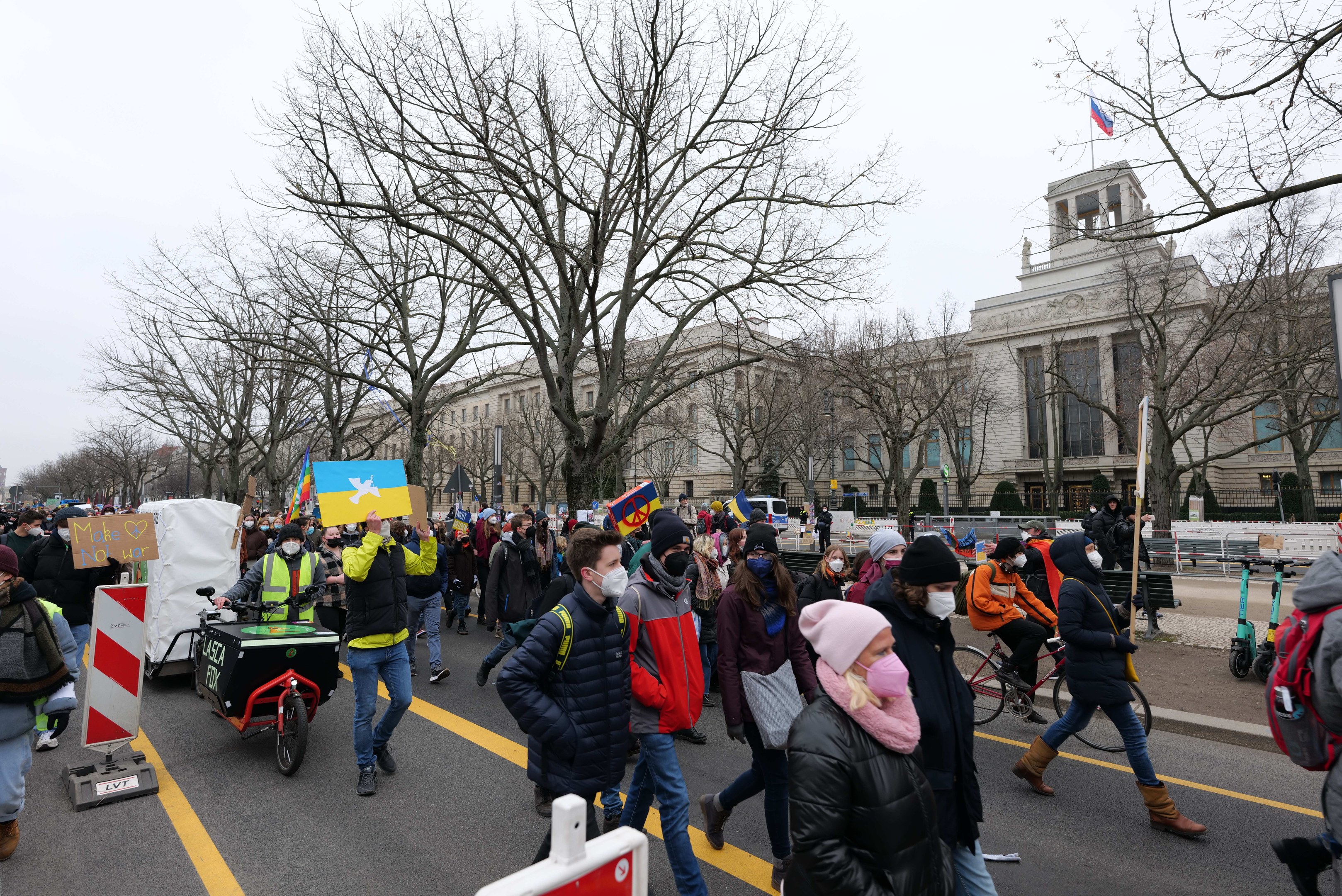 Eine große Gruppe von Menschen nimmt an einer Protestdemo in Washington, D.C. am 21. Januar 2020 teil und marschiert eine Straße entlang mit Schildern, Bannern und Fahrrädern vor einem Hintergrund aus Schildern, Bäumen und einem klaren blauen Himmel.