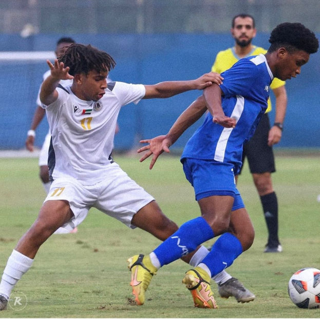 Zwei Männer beim Fußballspielen auf einem Rasenfeld, wobei einer zu siegen scheint.