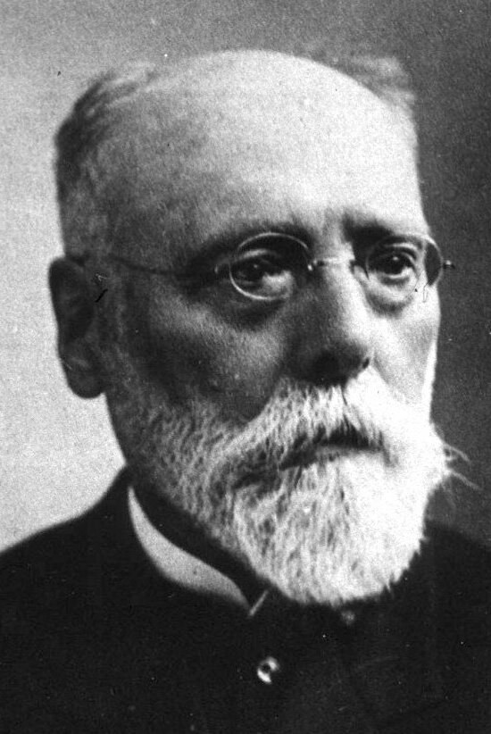 Schwarzes und weißes Porträt eines bärtigen Mannes in einem schwarzen Kleid und Brille mit ernstem Gesichtsausdruck, wahrscheinlich ein Soziologe.