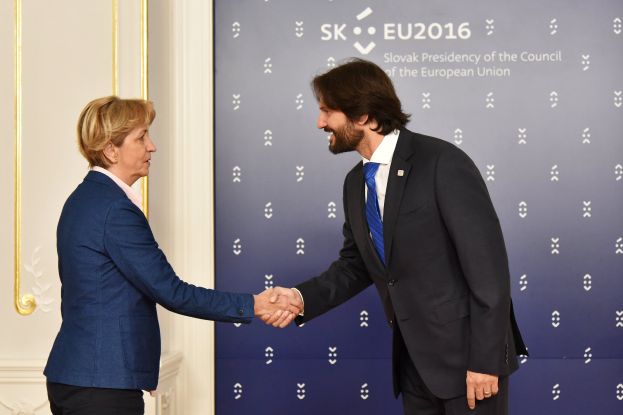 Bundeskanzlerin Angela Merkel und Bundespräsident Joachim Gauck schütteln Hände bei einem EU-Gipfeltreffen, lächeln und stehen vor einem Banner und einer Tür.