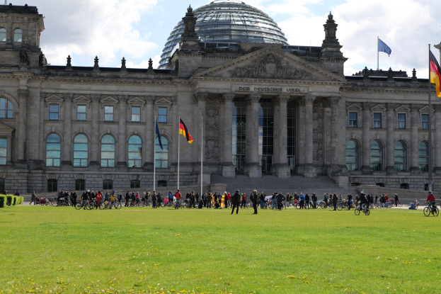 Eine Gruppe von Menschen, die vor dem Reichstaggebäude in Berlin Fahrrad fahren, mit seiner Kuppel, Säulen und flaggengeschmückten Umgebung.