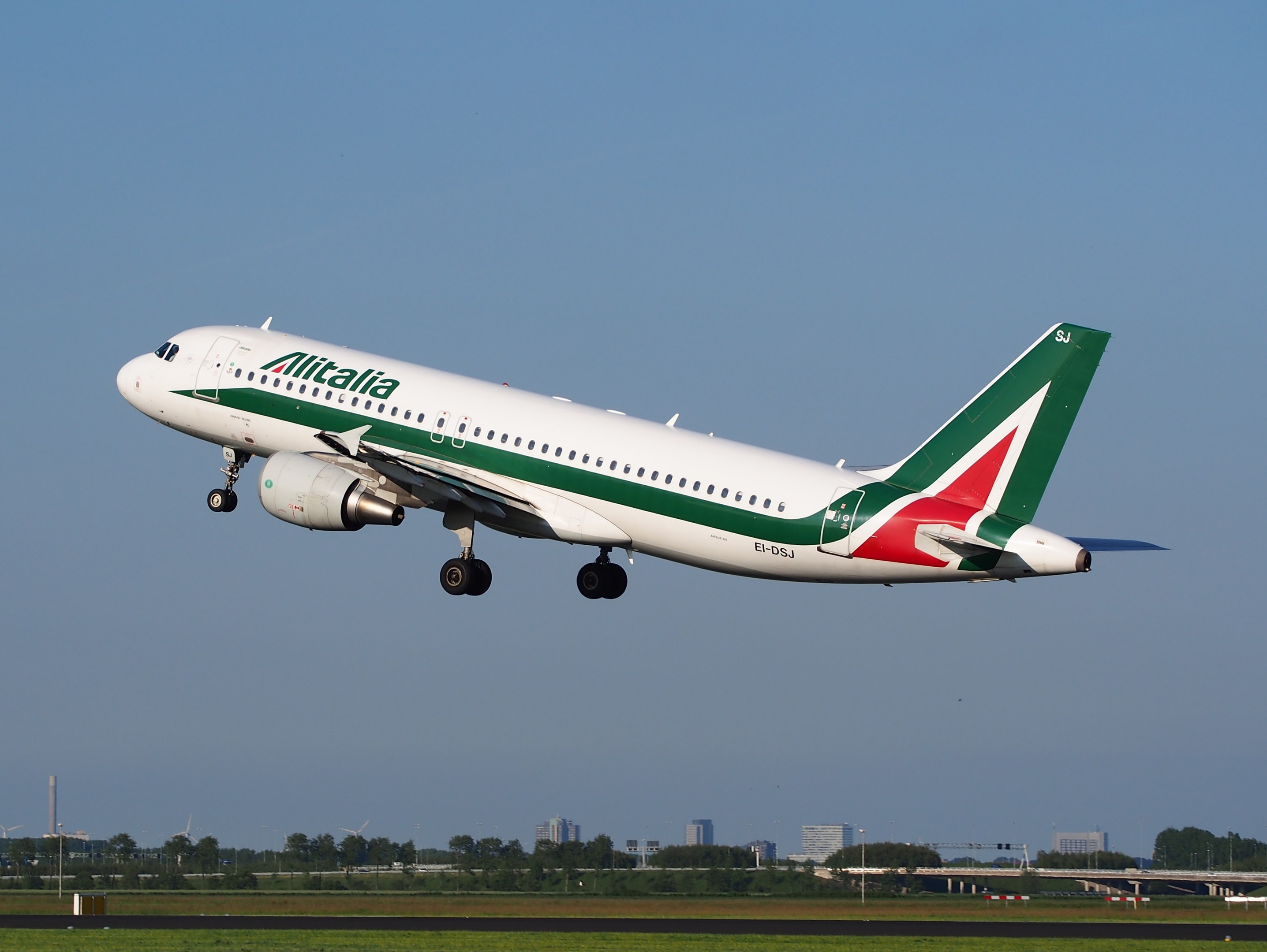 Alitalia Airbus A320-232 ERJ-EJZ Flugzeug beim Abheben vom Frankfurt Airport mit grünem Gras darunter, Bäumen und Gebäuden im Hintergrund und einem klaren blauen Himmel.