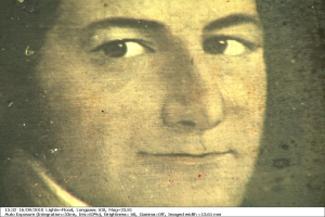 Schwarzes und weißes Foto einer Frau mit ernstem Gesichtsausdruck, direktem Blick, zurückgebundenem Haar und einem leichten Lächeln, mit Text unten.