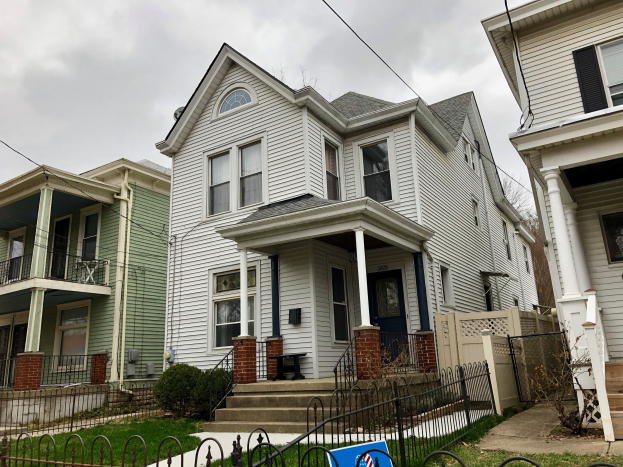 Reihe von Häusern mit Fenstern, Türen, Säulen, Geländern, Treppen und Dächern, umgeben von einem Metallzaun, Gras, Pflanzen, Bäumen und einem bewölkten Himmel, mit einem Mietschild unten, das die Adresse als 5901 S Elmwood Ave, Chicago 60618 angibt.