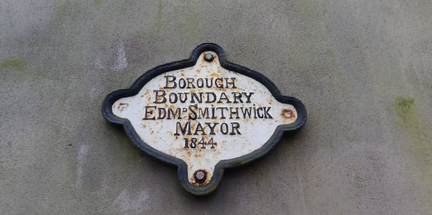 Metallschild an einem Gebäude mit schwarzem Hintergrund und weißer fettgedruckter Schrift, die "Stadtgrenze Edm Smithwick Bürgermeister" liest.