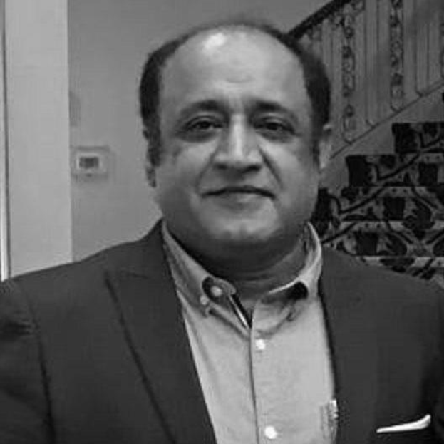 Ein Mann im Anzug steht vor einer Treppe, sieht besorgt aus, mit einer Wand im Hintergrund, dargestellt in Schwarz-Weiß.