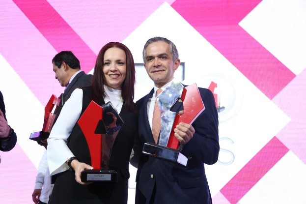 Zwei Personen auf einer Bühne mit Trophäen stehend und strahlend, mit einem Awards-Ceremony-Hintergrund.