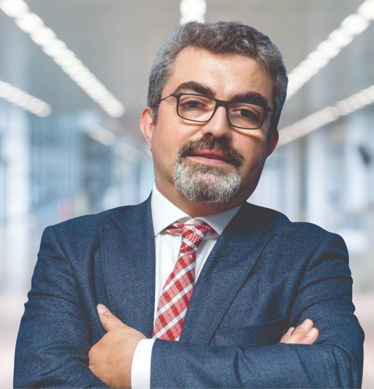 Ein Mann in Anzug und Krawatte mit verschränkten Armen und Brille steht vor einem unscharfen Hintergrund mit Text, der ihn als neu ernannte Marketingchef identifiziert.