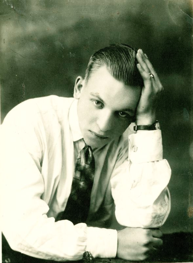 Ein Schwarz-Weiß-Foto eines Mannes in Hemd, Krawatte und einer Uhr am Handgelenk.