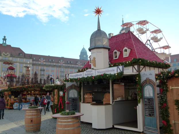 Ein geschäftiger Weihnachtsmarkt in Nürnberg, Deutschland, mit Menschen um dekorierte Stände, festliche Lichter, Schmuck, ein Riesenrad im Hintergrund, Gebäuden mit Fenstern und einem bewölkten Himmel, mit einer Tafel mit Text auf der rechten Seite.