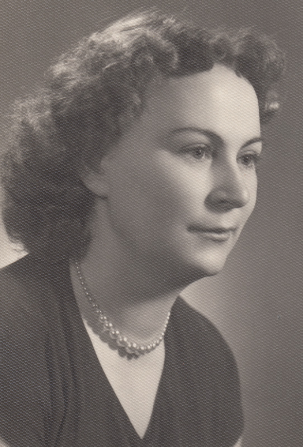 Ein Schwarz-Weiß-Foto einer Frau mit ernstem Gesichtsausdruck, die eine Kette und ein einfaches Kleid mit hohem Kragen und langen Ärmeln trägt, ihr Haar ist zurückgebunden und ihre Augen sind fokussiert.