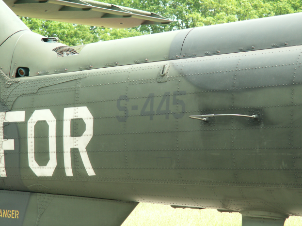 Nahaufnahme eines Militärhubschraubers mit dem Wort "FOR" auf der Seite, vor einem Hintergrund aus Bäumen.