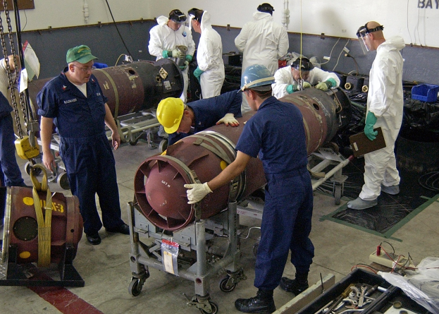 Männer in Helmen und Handschuhen, die eine große Bombe in einer Fabrik zerlegen.