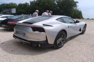 Roter Ferrari 812 Superfast auf der Goodwood Festival of Speed, umgeben von Menschen mit Mützen, Bäumen, Texttafeln und bewölktem Himmel im Hintergrund.