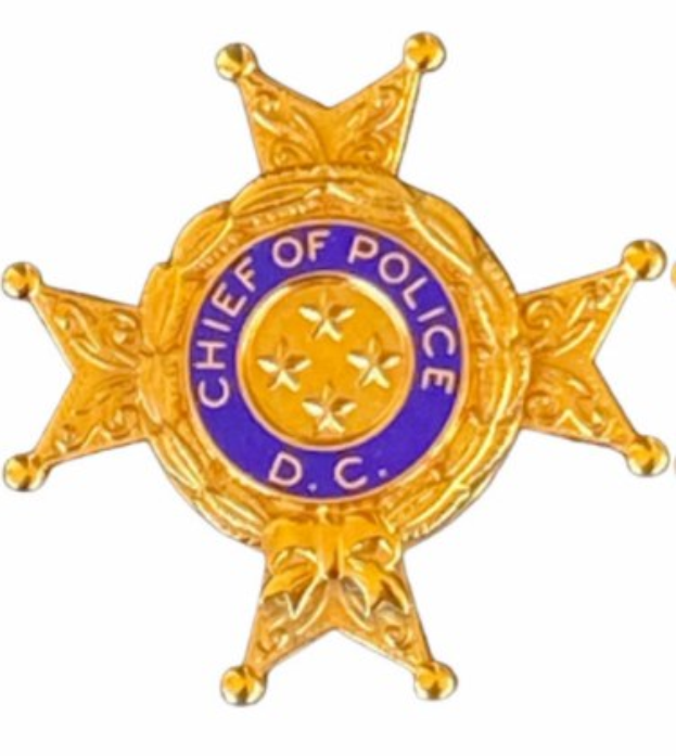 Eine goldene Polizei-Marke mit der Aufschrift "Polizeipräsident" auf einem weißen Hintergrund.