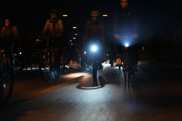 Eine Gruppe von Menschen, die nachts mit Fahrrädern auf einer Straße fahren, Helme tragen und von Straßenlaternen beleuchtet werden.