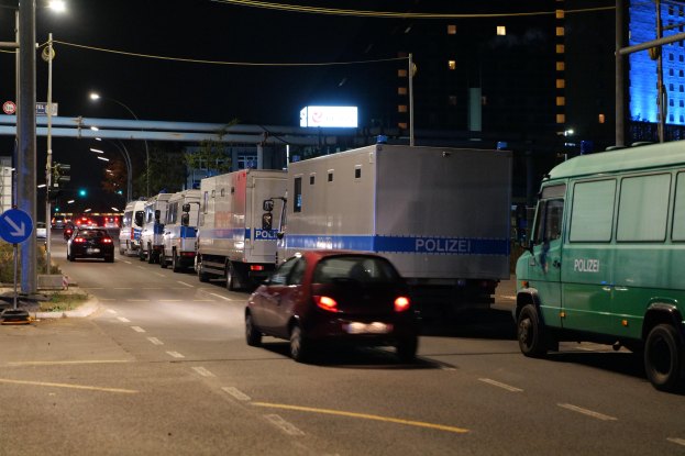 Lange Reihe von Polizeiwagen und -fahrzeugen, die an einer Straße bei Nacht geparkt sind, mit Verkehr, Straßenschildern, Versorgungsmasten, Gebäuden im Hintergrund.